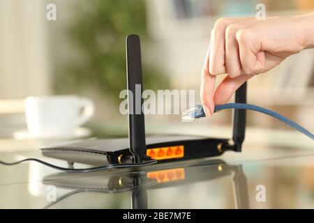 Nahaufnahme der Hände einer Frau, die das ethernet-Kabel an den Router auf einem Schreibtisch zu Hause anschließt Stockfoto