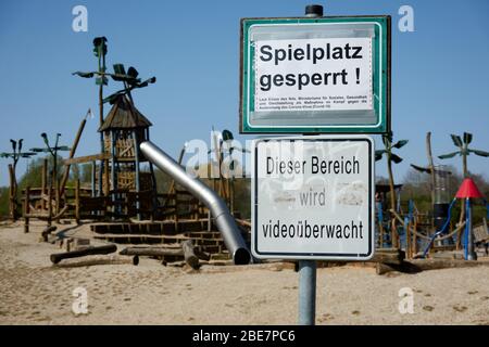 Schild mit der deutschen Aufschrift: "Spielplatz geschlossen, dieser Bereich wird durch Video überwacht" vor dem Eingang eines Abenteuerspielplatzes. Stockfoto