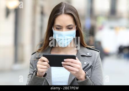 Ernste Frau mit Schutzmaske Vermeidung von Ansteckung beim Ansehen von Videos online auf dem Smartphone auf der Straße Stockfoto