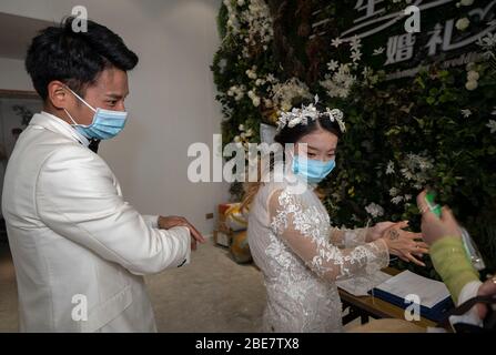 (200413) -- WUHAN, 13. April 2020 (Xinhua) -- Luo Jian (L) und Cheng Yishuang werden vor der Tür eines Fotostudios in Wuhan, Zentralchina, Provinz Hubei, am 12. April 2020 desinfiziert. Luo Jian und Cheng Yishuang hatten geplant, Hochzeitsfotos zu machen und eine Hochzeitszeremonie in Wuhan nach dem Frühlingsfest abzuhalten, das am 25. Januar dieses Jahres fiel, aber der Plan wurde unerwartet durch die COVID-19-Epidemie unterbrochen. Als die Coronavirus-Epidemie nachgab, hat Wuhan seit dem 3. April den Ehebuchdienst für Bürger wieder aufgenommen. Verwandte Branchen wie Kleid Vermietung und Hochzeit Fotografie auch sein Stockfoto