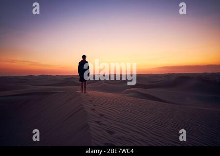 Einsamer Mann, der in der Dämmerung auf Sanddüne mitten in der Wüste steht. Abu Dhabi, Vereinigte Arabische Emirate Stockfoto