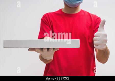 Mann aus dem Lieferservice in rotem T-Shirt, mit Schutzmaske und Handschuhen, die Pizza Box halten Stockfoto