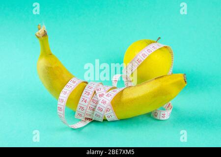 Verschiedene Arten von Obst, wie Äpfel und Bananen liegen auf einem Fuß und sind in einem Maßband verpackt - Konzept für eine gesunde Gewichtsabnahme Stockfoto