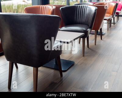 Lederstühle im Retro-Stil, orange und schwarze Farben und leerer Holztisch auf Holzfußboden im Café. Stockfoto