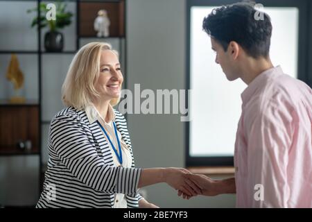 Freut mich, Sie kennenzulernen. Blonde Psychologin trifft ihren jungen männlichen Patienten in ihrem Büro und lächelt Stockfoto