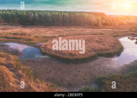 Der gewundene Bach fließt bei Sonnenuntergang durch die Wiese. Luftaufnahme. Ländliche Abendlandschaft Stockfoto