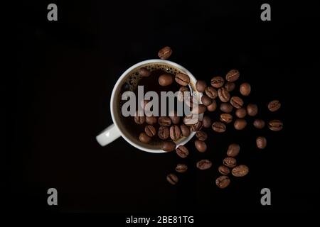 Kaffeebohnen schweben über Kaffeetasse isoliert auf schwarzem Hintergrund Stockfoto