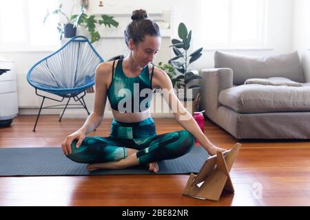 Kaukasische Frau Stretching zu Hause während Coronavirus Covid19 Pandemie und mit digitalen Tablet Stockfoto