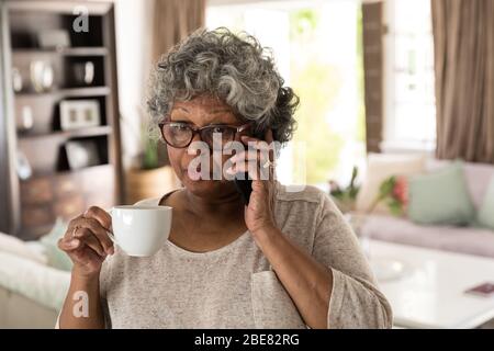 Eine ältere afroamerikanische Frau, die Zeit zu Hause verbringt und ein Getränk genießt Stockfoto