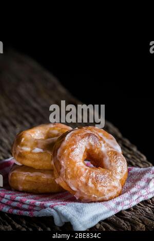 Ein glasierte Donuts auf einem rustikalen Holzbrett mit Kopierraum gestapelt. Dunkle Lebensmittel-Fotografie Stockfoto