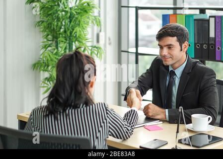 Junge Arbeitgeber in schwarzen Anzügen schütteln die Hände während eines Treffens im Büro. Angenehme Atmosphäre nach einem Vorstellungsgespräch. Stockfoto