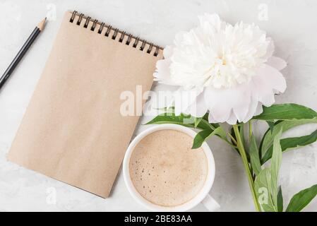 Morgen Tasse Kaffee, Papier Notizbuch und weiße Pfingstrose Blume auf Beton Tisch. Flach legen. Mock up. Draufsicht mit Kopierraum Stockfoto
