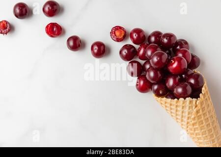 Frische Kirschenbeeren in Waffel Eis-Kegel auf weißem Marmor Hintergrund. Sommer Food Konzept. Draufsicht. Flach legen Stockfoto