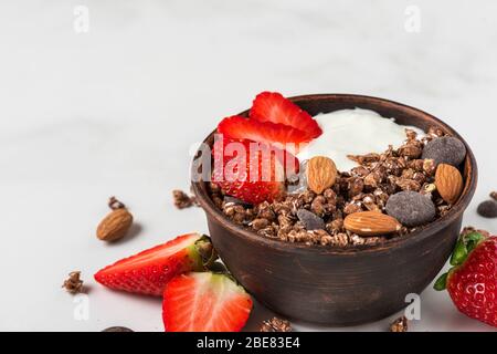 Gesundes Diät-Frühstück. Schüssel Haferschokolade Müsli mit Joghurt, frischen Erdbeeren und Mandeln auf weißem Marmortisch. Nahaufnahme Stockfoto