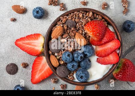 Gesundes Diät-Frühstück. Schüssel Haferschokolade Müsli mit Joghurt, frischen Beeren und Mandeln auf grauem Tisch. Draufsicht Stockfoto