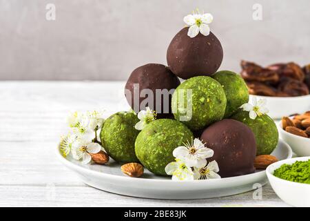 Grüne Matcha-Energiebälle oder Energiebeiße mit Energiebällen in Schokoladenglasur mit Frühlingsblumen. Gesunde vegane Diät Snacks. Food Styling. Nahaufnahme Stockfoto