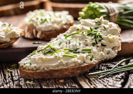 Nahaufnahme der Brotscheibe mit traditionellem slowakischen Bryndza-Aufstrich aus Schafskäse mit frisch geschnittenem Schnittlauch auf rustikalem Holz. Stockfoto