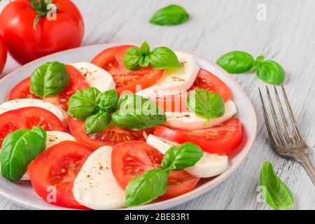 Caprese-Salat mit reifen Tomaten und Mozzarella-Käse mit frischen Basilikumblättern in einem Teller mit Gabel. Italienische Küche. Aussicht von oben Stockfoto
