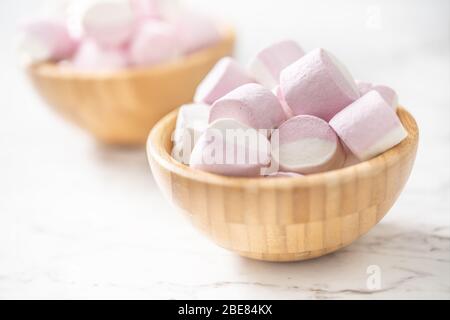 Rosa und weiße Marshmallows in einer vollen Holzschalen auf einer Marmoroberfläche mit einem Fokus auf die Schüssel in der Vorderseite platziert. Stockfoto