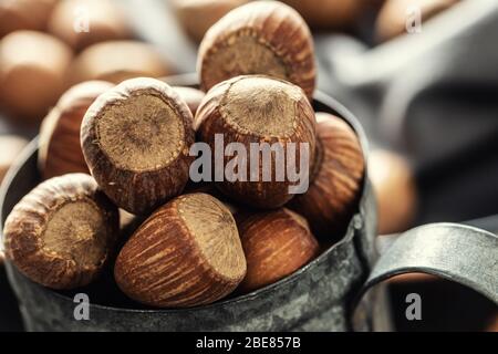 Nahaufnahme eines Vintage-Metallic-Becher voller Haselnüsse mit mehr Nüssen auf einem textilen Tischtuch um ihn herum. Stockfoto