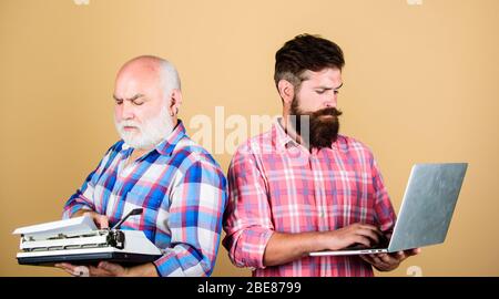 Mitbewerber: Vater und Sohn, Familiengeneration, Technologiekampf. Modernes Leben: Retro-Schreibmaschine im Vergleich zum Laptop. Neue Technologie. Jugend vs. Alter. Geschäftsansatz. Zwei bärtige Männer. Vintage-Schreibmaschine. Stockfoto