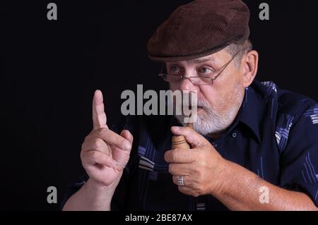 Künstlerisches Porträt eines bärtigen älteren Mannes, der Tabakpfeife hält und Zeigefinger vor schwarzem Hintergrund zeigt Stockfoto