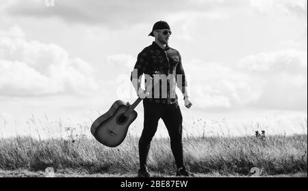 Landhausstil. Sommer Urlaub. Wandern Song. Inspiriert land Musiker. United mit der Natur. Stattlicher Mann mit Gitarre. Country Music Konzept. Gitarrist Land Sänger stand im Feld Himmel Hintergrund. Stockfoto
