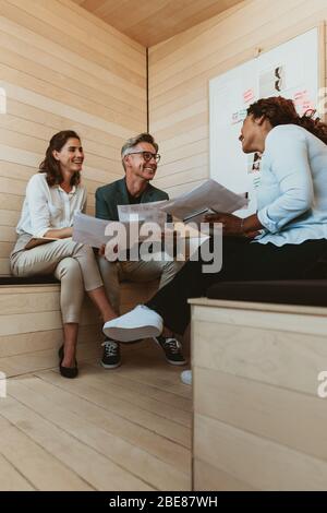 Designerin, die ihrem Team bei der Besprechung neue Ideen zum Projekt gibt. Geschäftsleute diskutieren über neue Geschäftsprojekten im Büro. Stockfoto