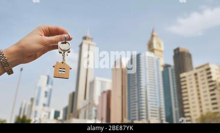 Konzept des Immobilienkaufs. Das Mädchen hält die Schlüssel zu einem neuen Haus auf dem Hintergrund eines Wolkenkratzers in Dubai. Stockfoto