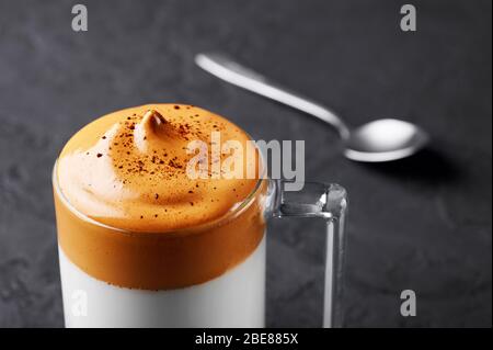 Dalgona Kaffee in einer transparenten Tasse an schwarzer Schieferplatte. Dalgona Schaumkaffee ist ein südkoreanisches Getränk mit Schlagsahne, Zucker und Mill Stockfoto