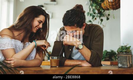 Lächelnder Mann und Frau, die Kaffee aus demselben Glas mit Stroh trinken und lächeln. Junges Paar, das einen Kaffee in einem Café genießt. Stockfoto