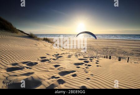 Mann mit Paragleiter am Strand am Meer bei Sonnenuntergang Stockfoto