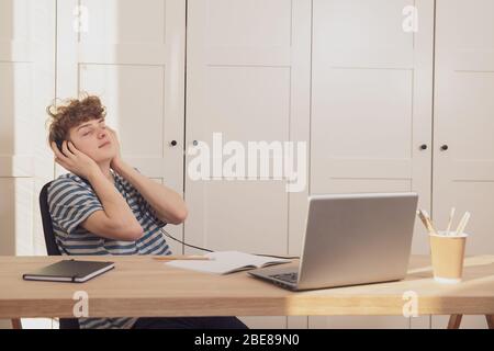 Ein Teenager hört sich in Kopfhörern entspannende Musik an, benutzt einen Laptop und ruht sich aus. Er macht eine Pause vom Studium Stockfoto
