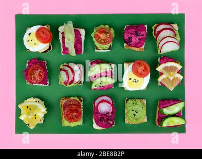 Set verschiedene Bruschetta Sandwiches mit Rübenhummus, Guacamole, verschiedene Gemüse. Vegetarisches Helsifood-Konzept. Sommernack. Food patern auf gree Stockfoto