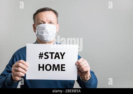 Erwachsener Mann in schützende medizinische Maske hält weiße leer für Text - ZU HAUSE bleiben. Covid-19. Quarantänekonzept. Coronavirus-Prävention. Stockfoto