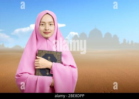 Asiatische Muslimin in einem Schleier stehend und hält den Koran auf der Düne Stockfoto