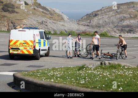 Bild: Eine Gruppe von Kindern auf dem Fahrrad wird von einem Polizisten auf dem ansonsten menschenleeren Parkplatz Bracelet Bay in der Nähe von Swansea, Wales, Großbritannien, angesprochen. Stockfoto