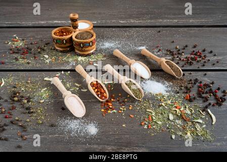 Verschiedene Gewürze und in Holzlöffel. Flacher Gewürzlack Zutaten Chili, Salz, himalaya-Salz, herzhaft und schwarzer Pfeffer auf grauem Holzbrett. Stockfoto