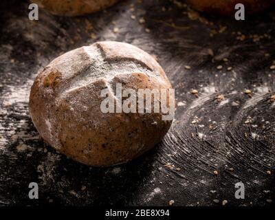 Das rustikale Brot auf schwarzem Holzhintergrund gelegt. Morgens Brötchen mit Sonneneinstrahlung in der Nähe. Stockfoto