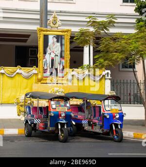 Bangkok, Thailand - 29. Februar 2020:zwei 'Tuk-Tuks' (Thailands berühmte altmodische Taxis) parken vor dem Porträt des thailändischen Königs. Stockfoto