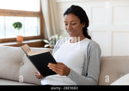Ruhiges afroamerikanisches Mädchen lächelt und liest ein Buch Stockfoto