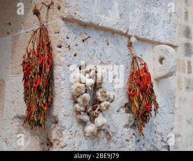 Vor einem Haus hängen Trauben von getrockneten Chilis und Knoblauch, um sie an einer weiß getünchten Wand zu trocknen Stockfoto