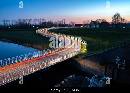 Geschwungene asphalanische Landstraße in holländischer Landschaft mit weißem Zaun, der zu einem alten Bauernhaus in Holland führt. Stockfoto