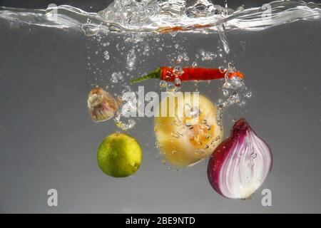 Foto von roten Zwiebeln, roten Chili, Knoblauch, Tomaten und Calamansi in Wasser fallen gelassen Stockfoto