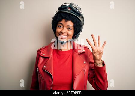 Junge afro amerikanische Afromotorradfahrerin Frau mit lockigen Haaren trägt Motorradhelm zeigt und zeigt mit den Fingern Nummer vier während Smilie Stockfoto