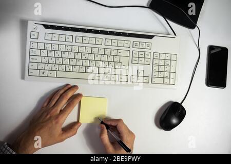 Ein Mann im Home Office schreibt abends eine Erinnerungsnotiz auf seinen Schreibtisch Stockfoto