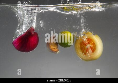 Foto von roten Zwiebeln, Knoblauch, Tomaten und Calamansi in Wasser fallen gelassen Stockfoto