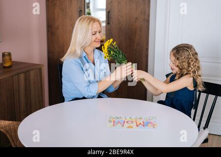 Liebevolle Tochter gibt Blumenstrauß Blumen zu ihrer Mutter. Mädchen gibt ein Geschenk an ihre geliebte Mutter. Stockfoto
