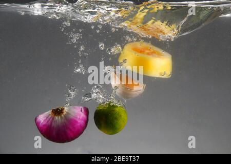 Foto von roten Zwiebeln, Knoblauch, Tomaten und Calamansi in Wasser fallen gelassen Stockfoto