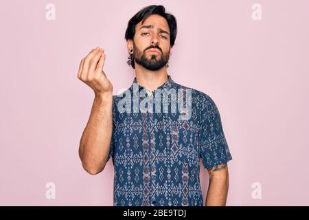 Junger gutaussehender hispanischer Bohemian Mann, der Hippie-Stil auf rosa Hintergrund mit italienischer Geste mit Hand und Fingern selbstbewussten Ausdruck trägt Stockfoto